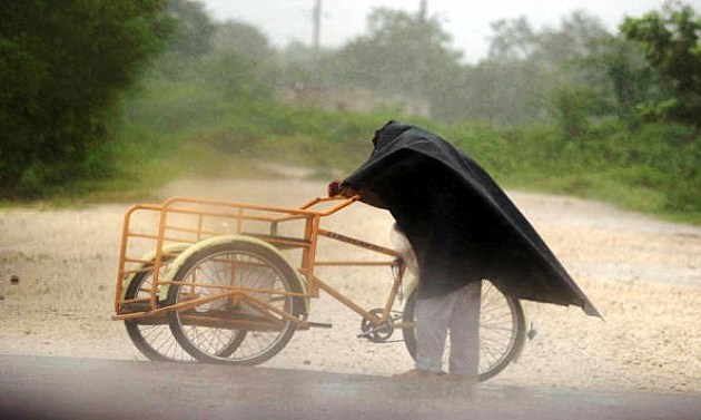 A street vendor tries to walk against the strong winds, he's struggling to ride his bike into the wind